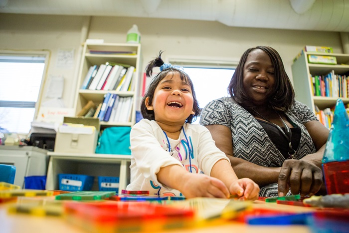 Young girl sits at a table with her woman teacher and smiles