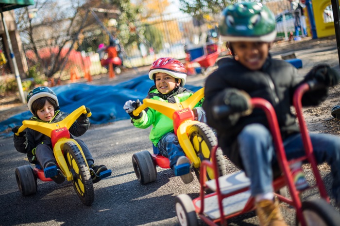 Children on colorful tricycles ride on a playground